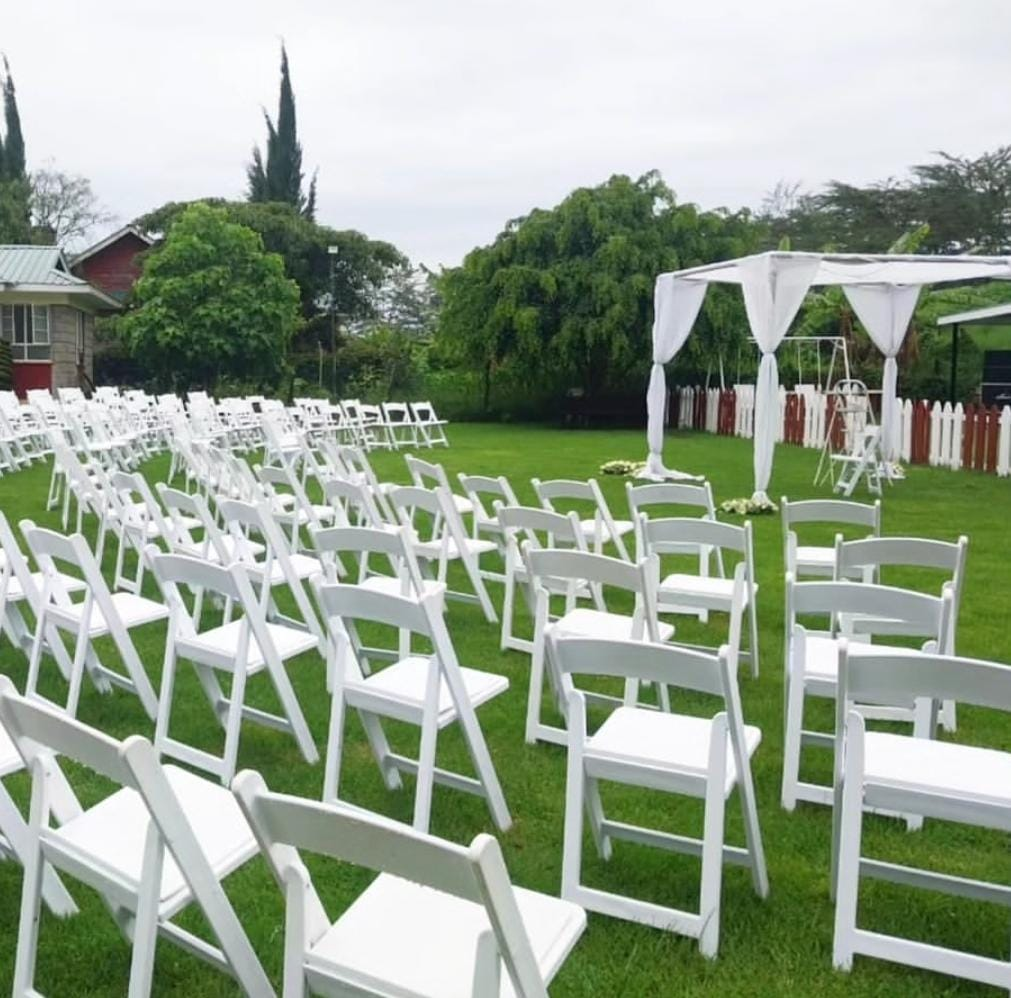 Garden wedding ceremony setup with white chairs and draped arch